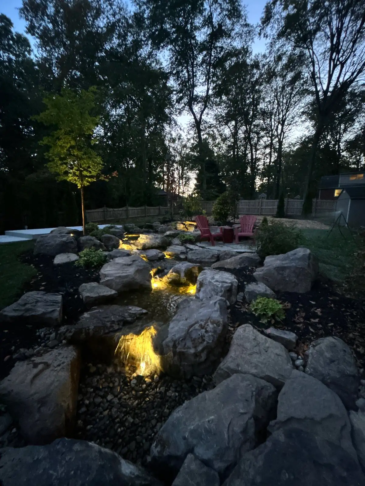 LED-lit waterfall and pond at night with natural boulders
